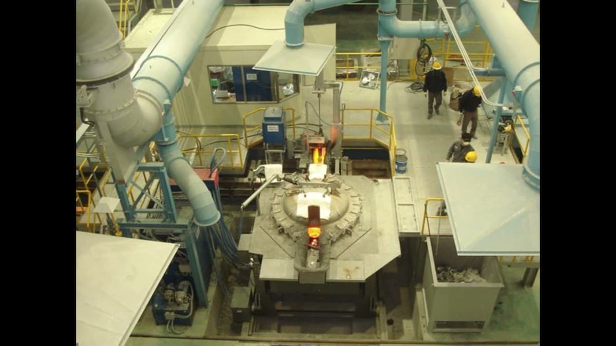 Overhead view of a coreless induction furnace installation in a CIME foundry, showing the yellow-hot molten bath and the fume-extraction ductwork