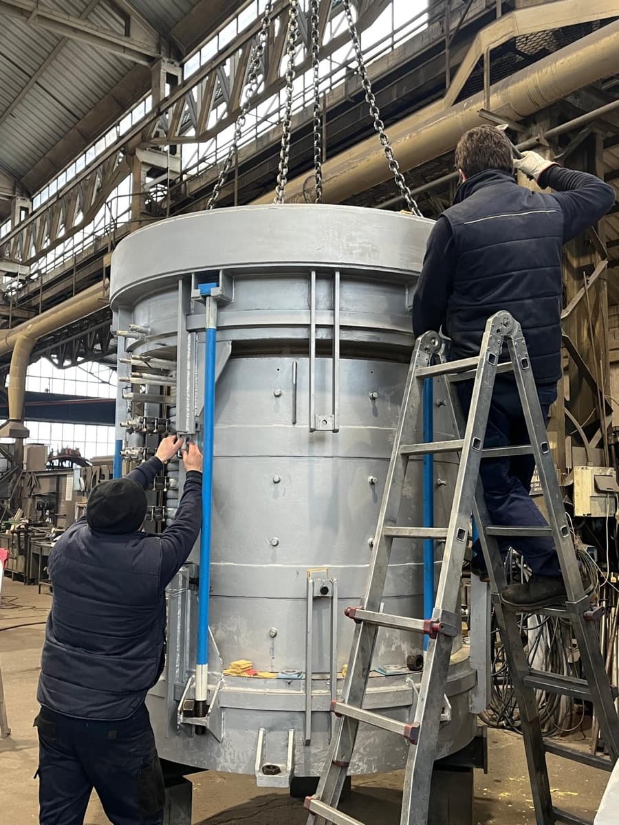 Two CIME technicians assembling a coreless furnace body, guiding the crucible top while adjusting the vertical magnetic-yoke clamping columns