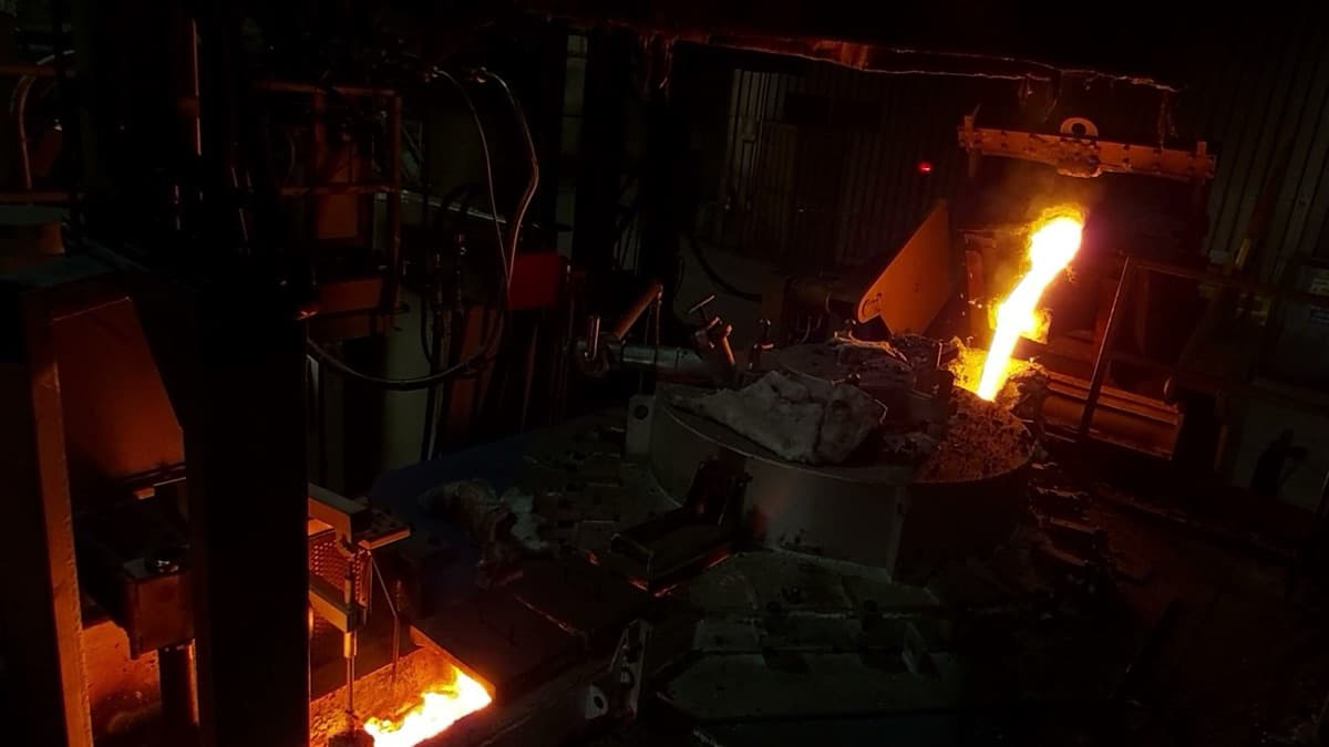 Molten ductile iron being charged into the sealed body of a CIME CAP press-pouring furnace from an overhead ladle in a darkened foundry